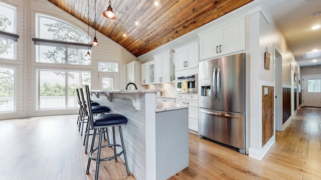 kitchen with an island with sink, stainless steel appliances, a kitchen breakfast bar, hanging light fixtures, and light wood-type flooring