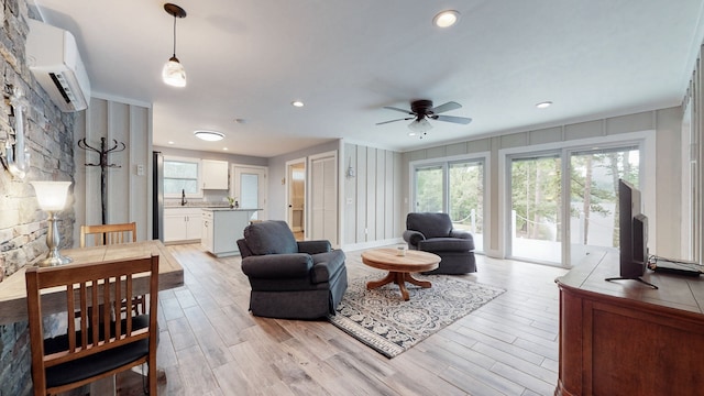 living room featuring a wall mounted AC, ceiling fan, and light wood-type flooring