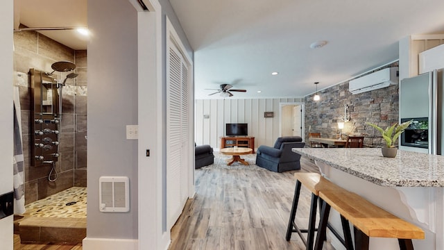 kitchen with a kitchen bar, ceiling fan, light wood-type flooring, and light stone counters