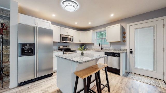 kitchen featuring a kitchen island, light hardwood / wood-style flooring, appliances with stainless steel finishes, white cabinets, and light stone counters