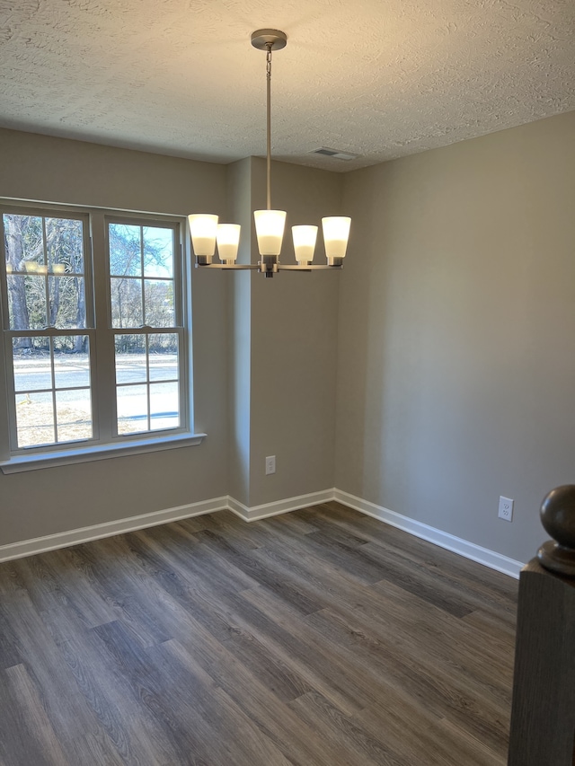 unfurnished dining area with a textured ceiling, dark wood-type flooring, and a notable chandelier