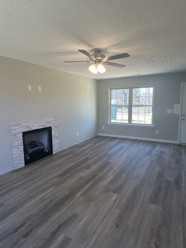 unfurnished living room with a textured ceiling, dark hardwood / wood-style flooring, a stone fireplace, and ceiling fan