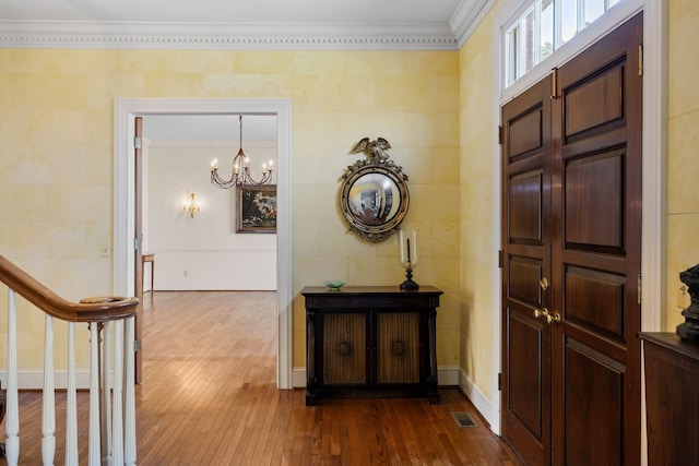 entrance foyer with tile walls, dark wood-type flooring, ornamental molding, and a notable chandelier