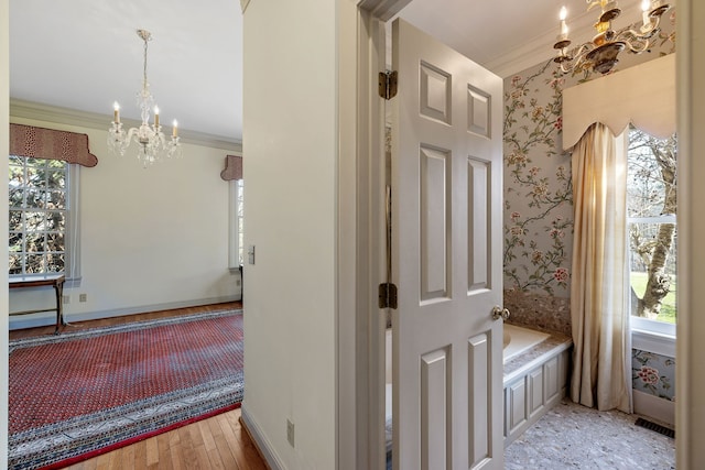 hallway with crown molding, light hardwood / wood-style floors, a notable chandelier, and a wealth of natural light