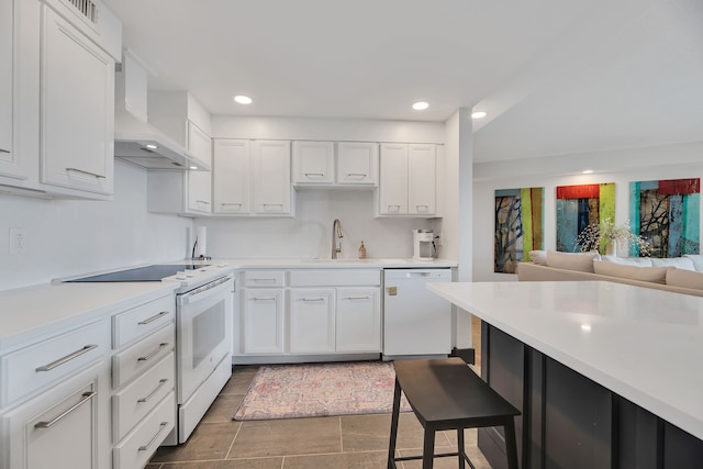 kitchen with wall chimney range hood, white appliances, dark tile flooring, sink, and white cabinetry