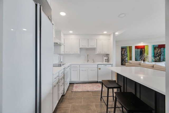 kitchen featuring a kitchen breakfast bar, white appliances, white cabinets, dark tile floors, and sink