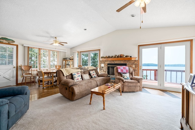 living room featuring a textured ceiling, a water view, lofted ceiling, and a fireplace