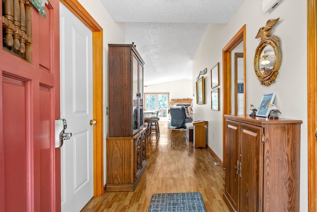 hall with vaulted ceiling, a textured ceiling, and light wood-type flooring