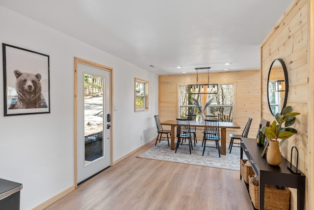 dining room featuring an inviting chandelier, wooden walls, and light hardwood / wood-style flooring