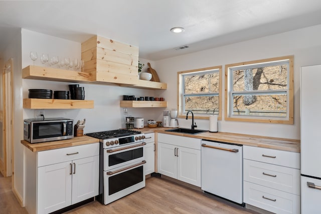 kitchen featuring white cabinets, butcher block countertops, light hardwood / wood-style floors, and white appliances