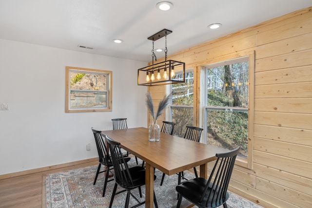 dining room featuring an inviting chandelier, wood walls, and light hardwood / wood-style floors