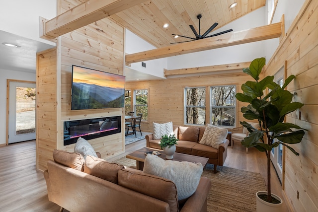 living room featuring wood walls, light hardwood / wood-style floors, ceiling fan, and high vaulted ceiling