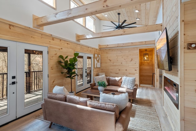 living room featuring french doors, wooden walls, ceiling fan, and light hardwood / wood-style flooring