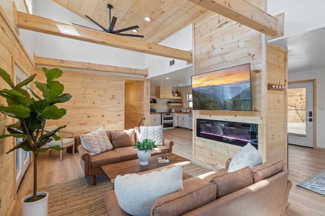 living room featuring ceiling fan, wood walls, light hardwood / wood-style floors, and plenty of natural light