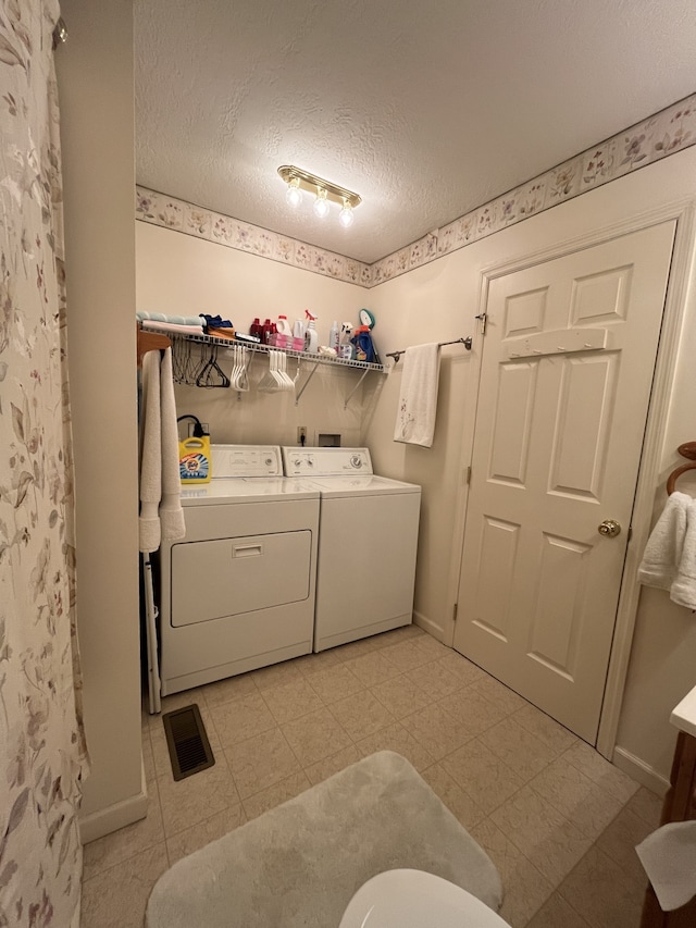 laundry room with a textured ceiling, washer and dryer, and light tile floors