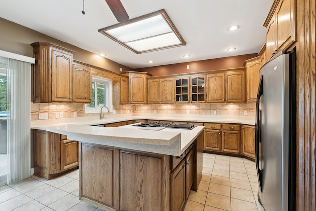 kitchen with light tile floors, a kitchen island, backsplash, and stainless steel refrigerator