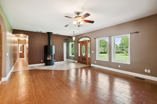 unfurnished living room featuring ceiling fan, a wood stove, and light wood-type flooring