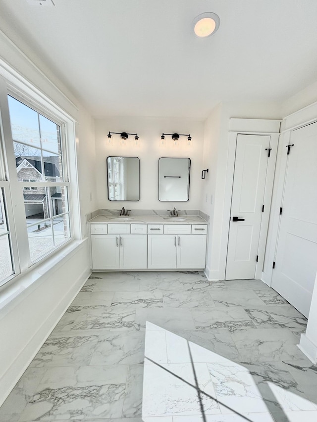 full bathroom with double vanity, marble finish floor, baseboards, and a sink