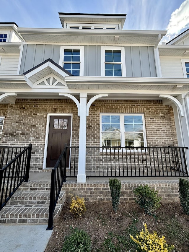 view of exterior entry featuring a porch, board and batten siding, and brick siding