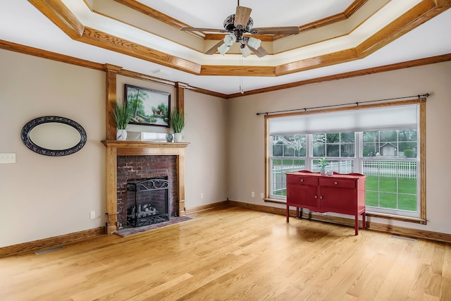 unfurnished living room featuring a tray ceiling, a fireplace, light hardwood / wood-style floors, and crown molding