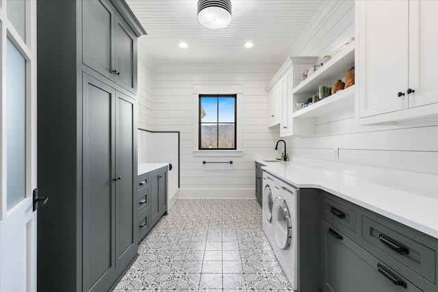 laundry room with wood walls, light tile floors, sink, washer and clothes dryer, and cabinets