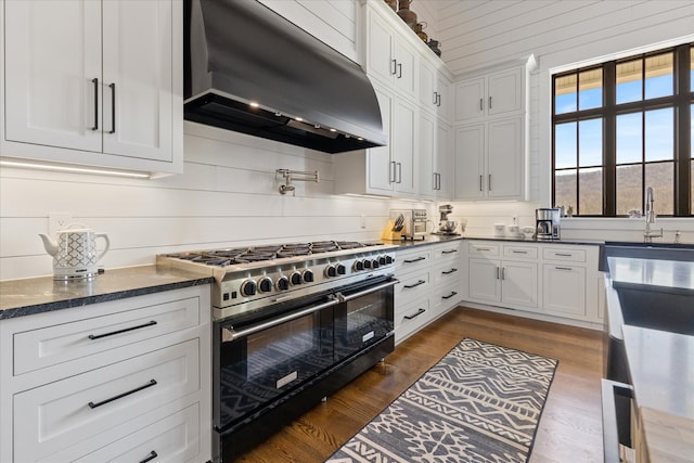 kitchen featuring range with two ovens, dark stone countertops, white cabinetry, wall chimney exhaust hood, and dark wood-type flooring