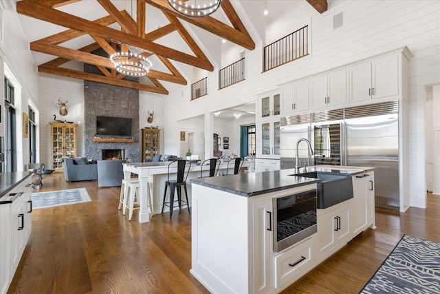 kitchen with white cabinets, dark hardwood / wood-style flooring, an island with sink, and a fireplace