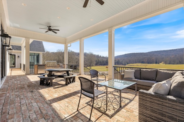 view of patio / terrace with a mountain view, ceiling fan, area for grilling, outdoor lounge area, and exterior kitchen