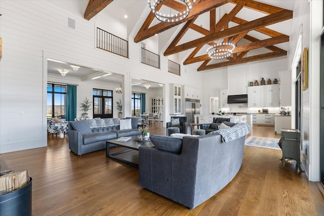 living room with a notable chandelier, hardwood / wood-style floors, a towering ceiling, and beam ceiling