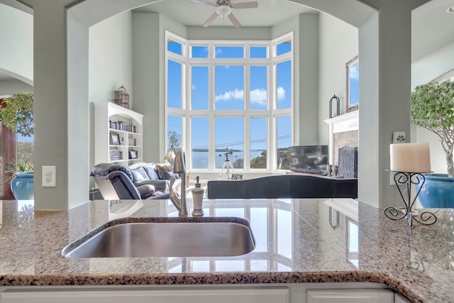 kitchen with a high ceiling, ceiling fan, sink, and light stone counters