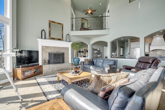 tiled living room with a brick fireplace, sink, ceiling fan, and a towering ceiling