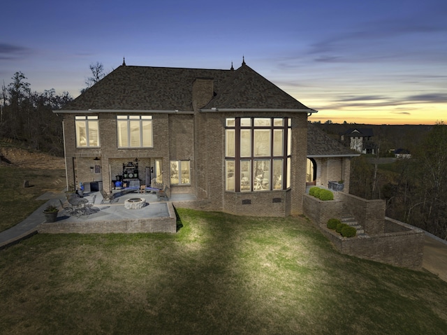 back house at dusk featuring a patio, an outdoor fire pit, and a lawn