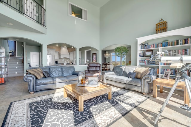 living room with a towering ceiling, a chandelier, light tile floors, and sink