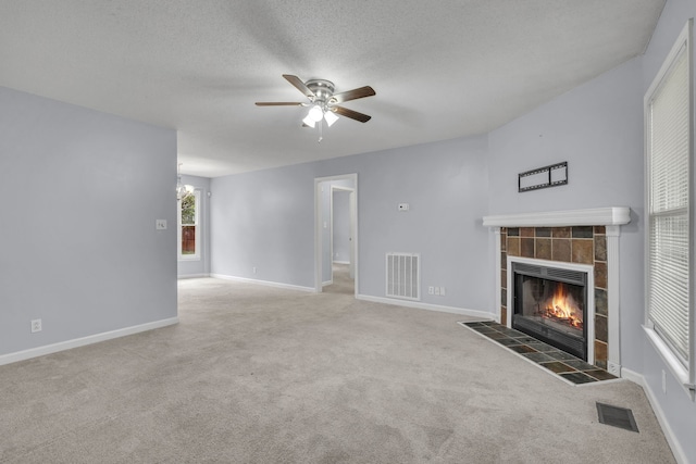 unfurnished living room featuring a textured ceiling, dark colored carpet, a fireplace, and ceiling fan with notable chandelier