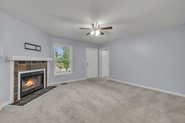 unfurnished living room featuring ceiling fan, a tiled fireplace, and light colored carpet