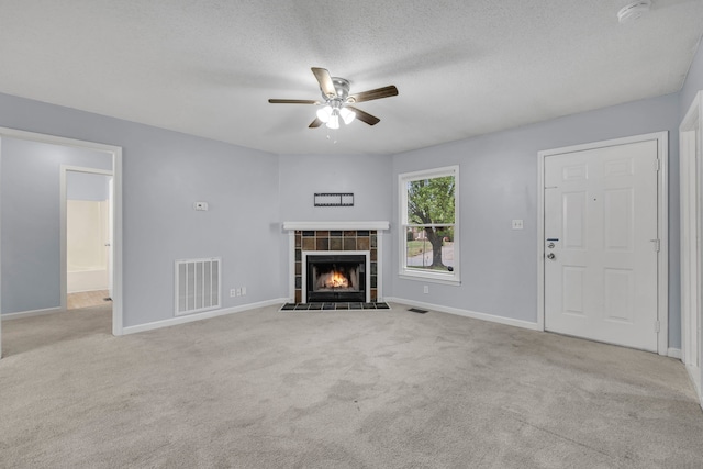 unfurnished living room featuring a tiled fireplace, light carpet, a textured ceiling, and ceiling fan