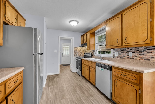 kitchen featuring appliances with stainless steel finishes, sink, light hardwood / wood-style flooring, a textured ceiling, and tasteful backsplash