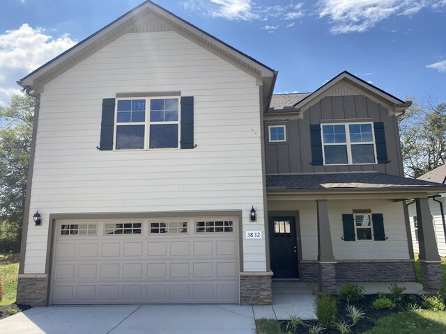 view of front of house with a porch, a garage, stone siding, driveway, and board and batten siding