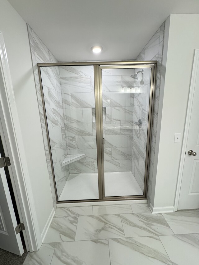 bathroom featuring marble finish floor, a shower stall, and baseboards