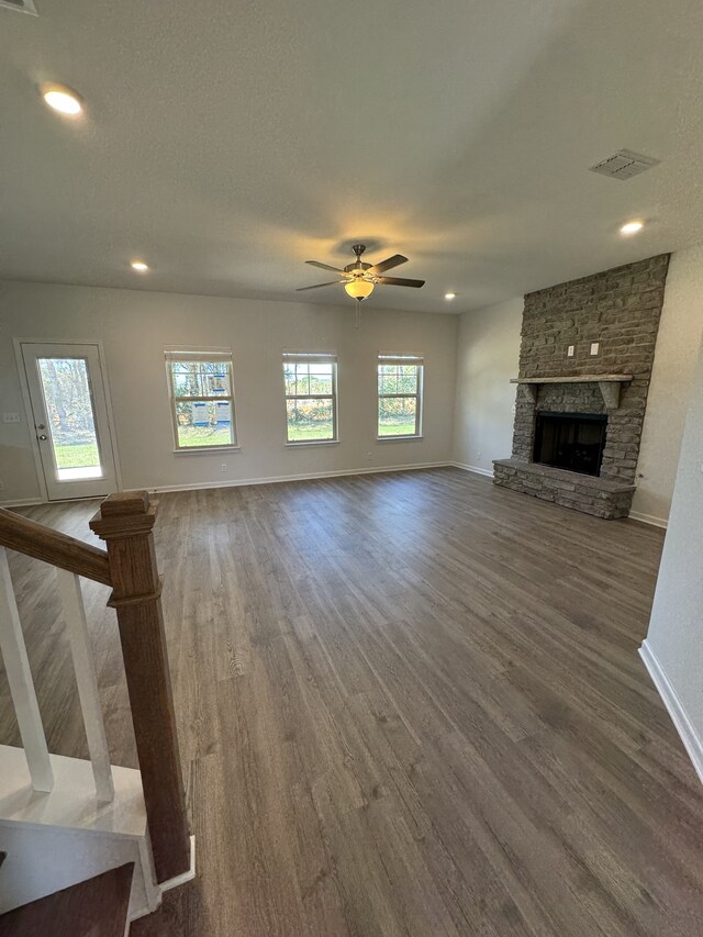 unfurnished living room featuring visible vents, baseboards, ceiling fan, wood finished floors, and a stone fireplace