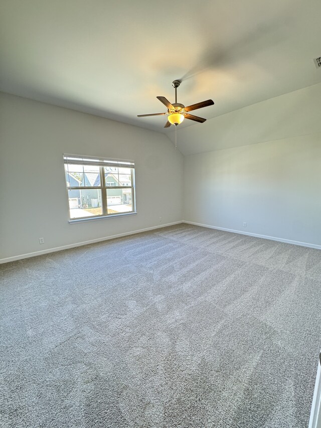 empty room with vaulted ceiling, carpet floors, ceiling fan, and baseboards