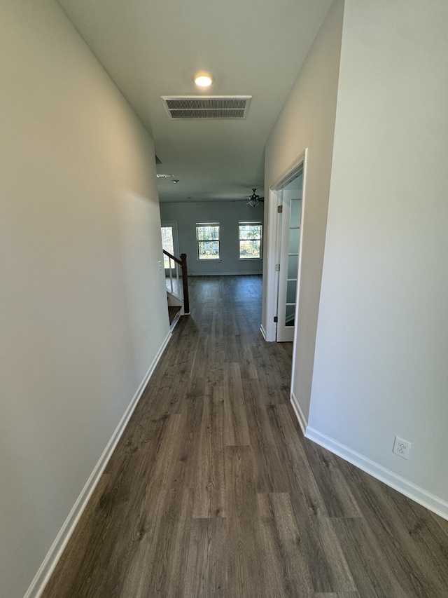 hall featuring dark wood-type flooring, baseboards, visible vents, and an upstairs landing