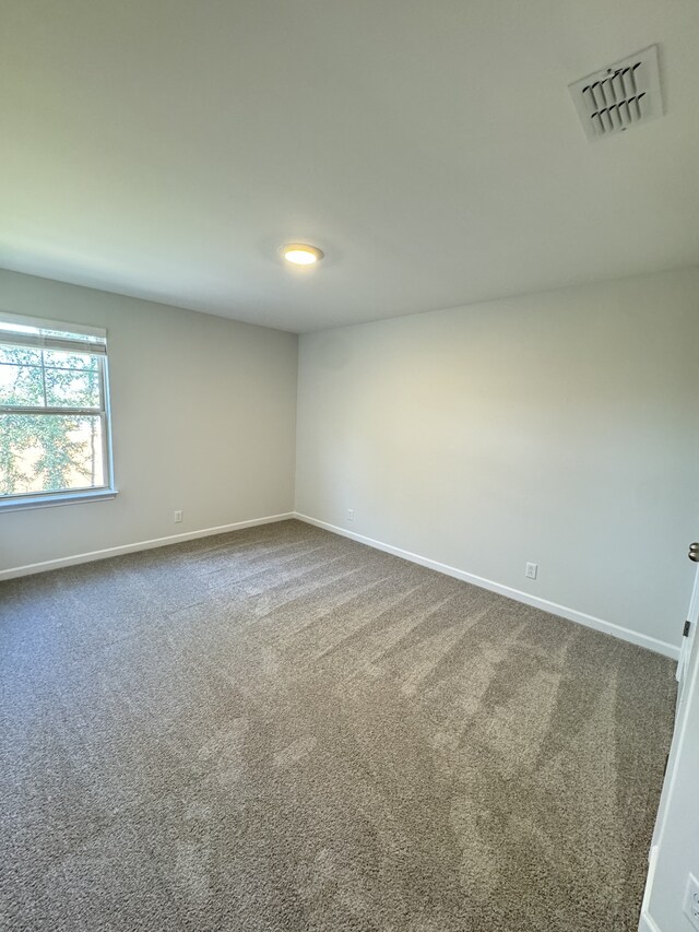 empty room with dark colored carpet, visible vents, and baseboards