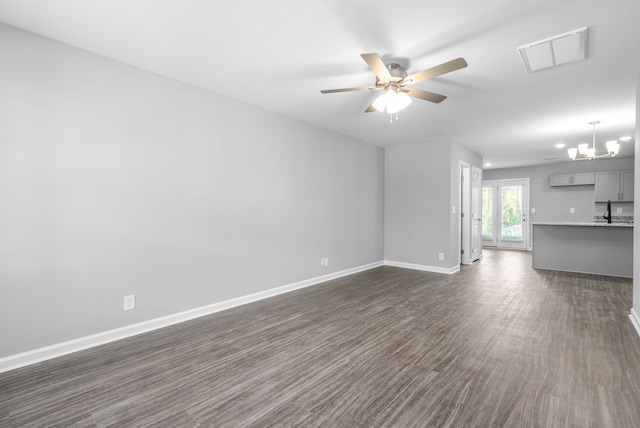 unfurnished living room featuring dark wood finished floors, ceiling fan with notable chandelier, visible vents, and baseboards