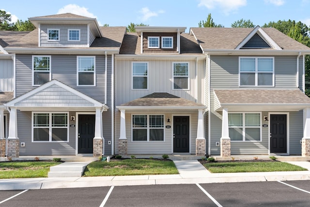 townhome / multi-family property featuring stone siding, uncovered parking, covered porch, and roof with shingles