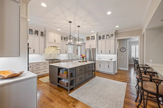 kitchen featuring a kitchen island with sink, backsplash, dark wood-type flooring, and white cabinetry