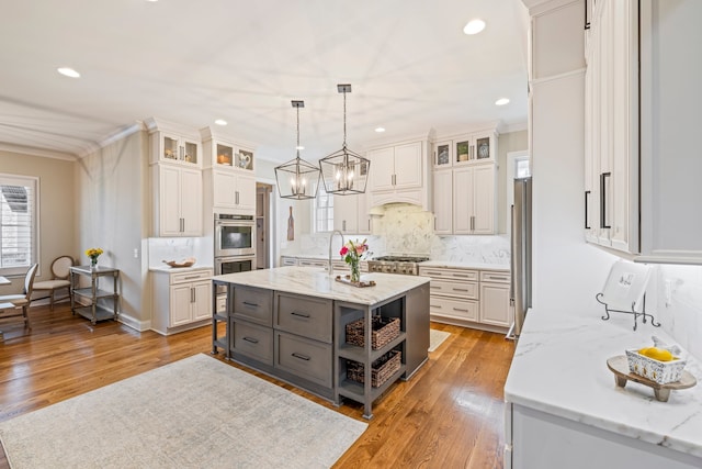 kitchen featuring gray cabinetry, an island with sink, light hardwood / wood-style floors, white cabinetry, and tasteful backsplash