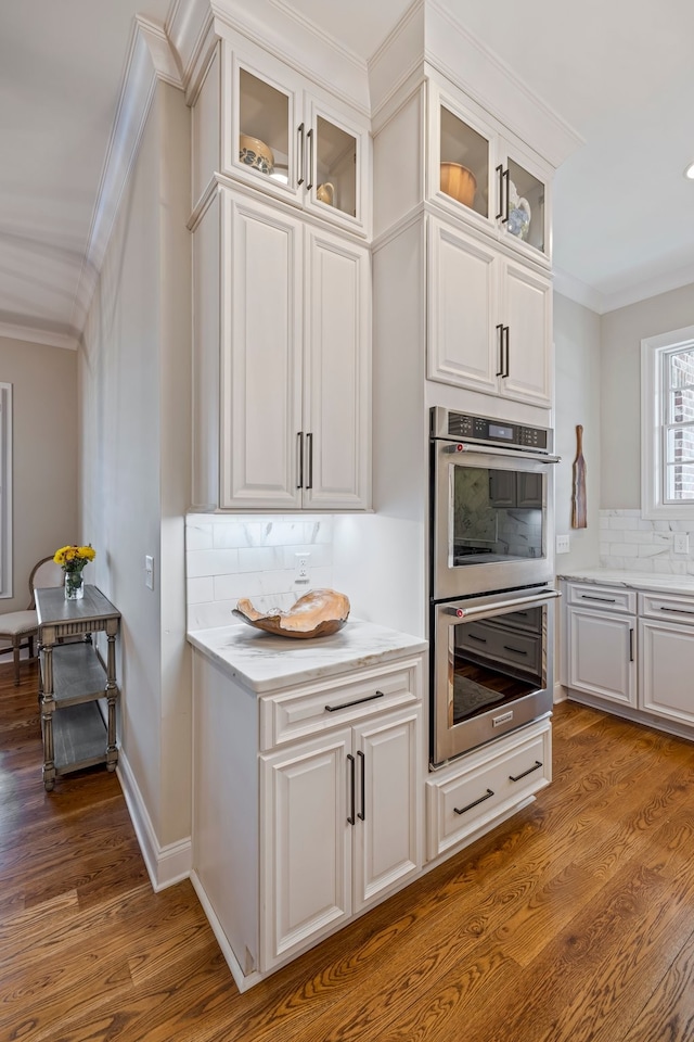 kitchen with dark wood-type flooring, backsplash, double oven, white cabinetry, and ornamental molding