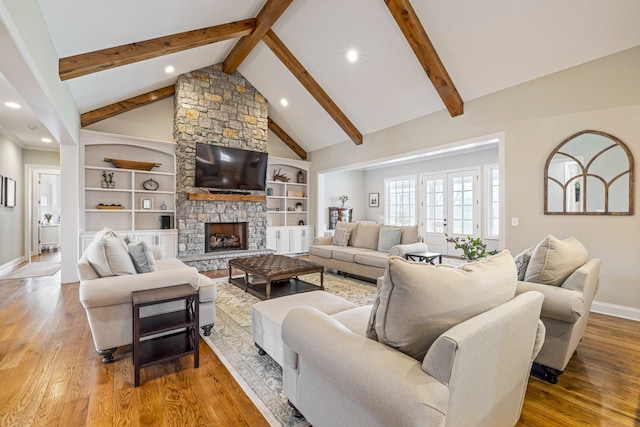 living room with light wood-type flooring, beam ceiling, a stone fireplace, high vaulted ceiling, and built in shelves