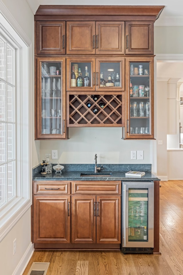 bar with sink, dark stone counters, light wood-type flooring, and wine cooler